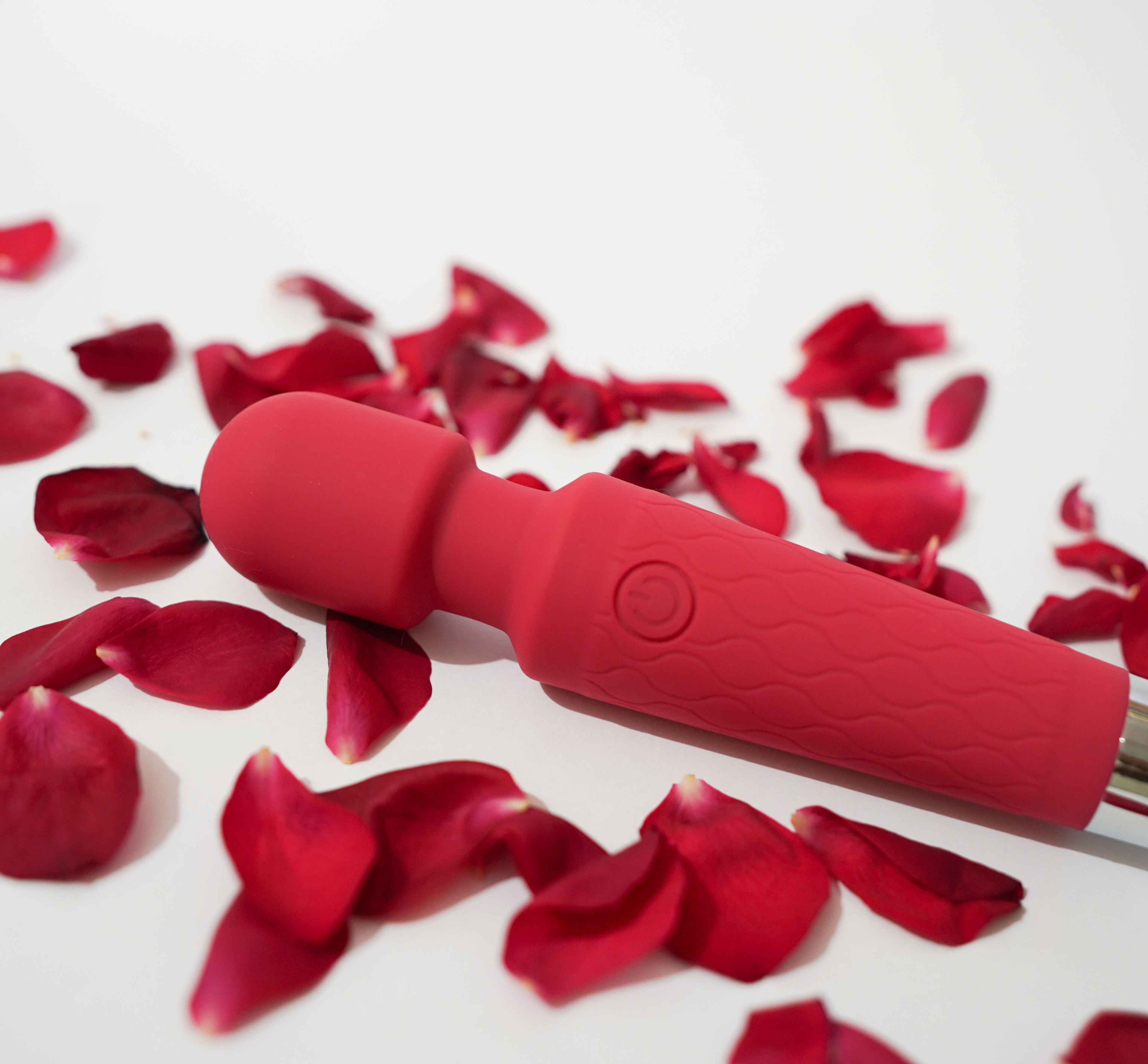 Libertee's red handheld massager device surrounded by red rose petals on a white background.