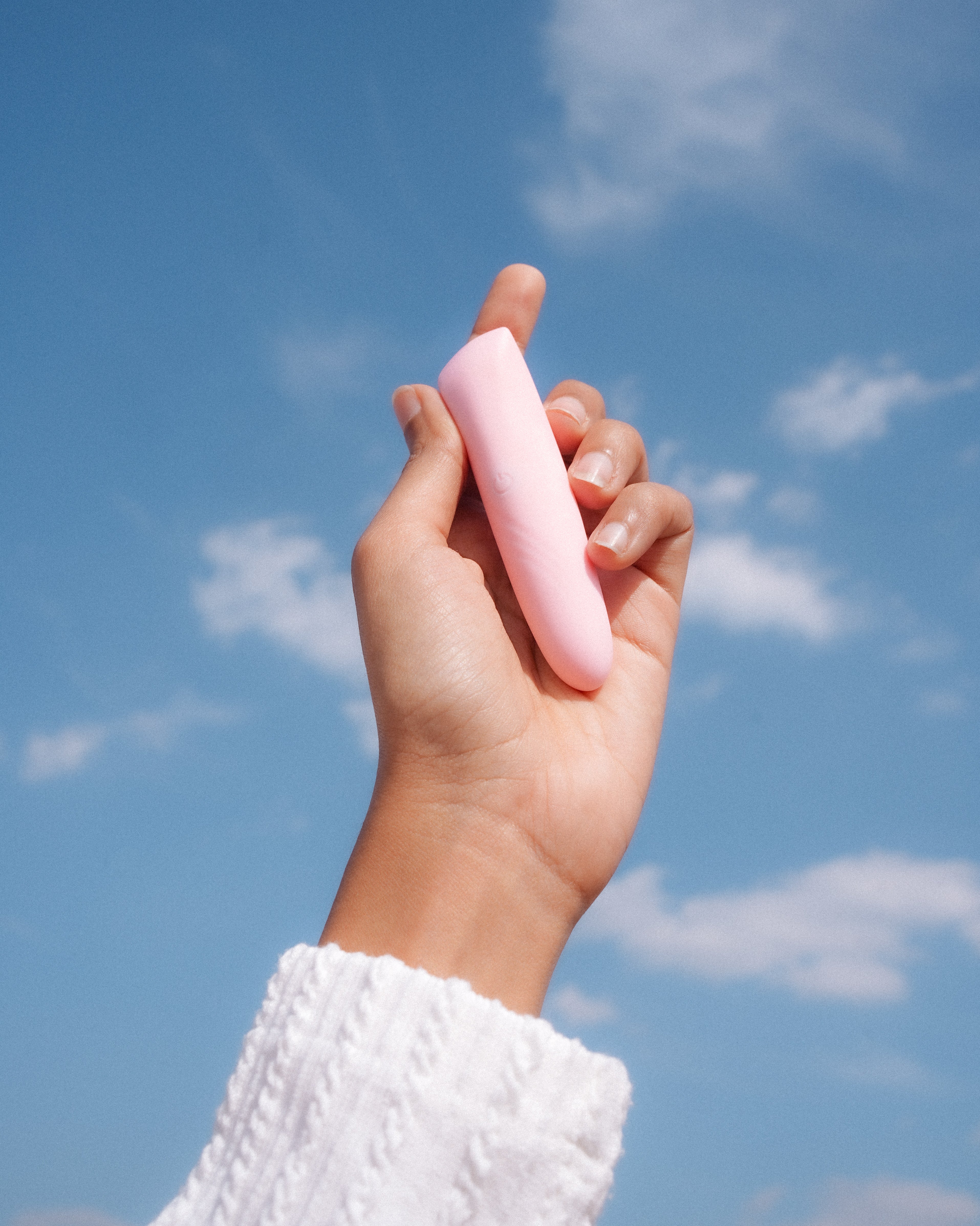 Hand holding a pink personal wellness massager against a blue sky with clouds
