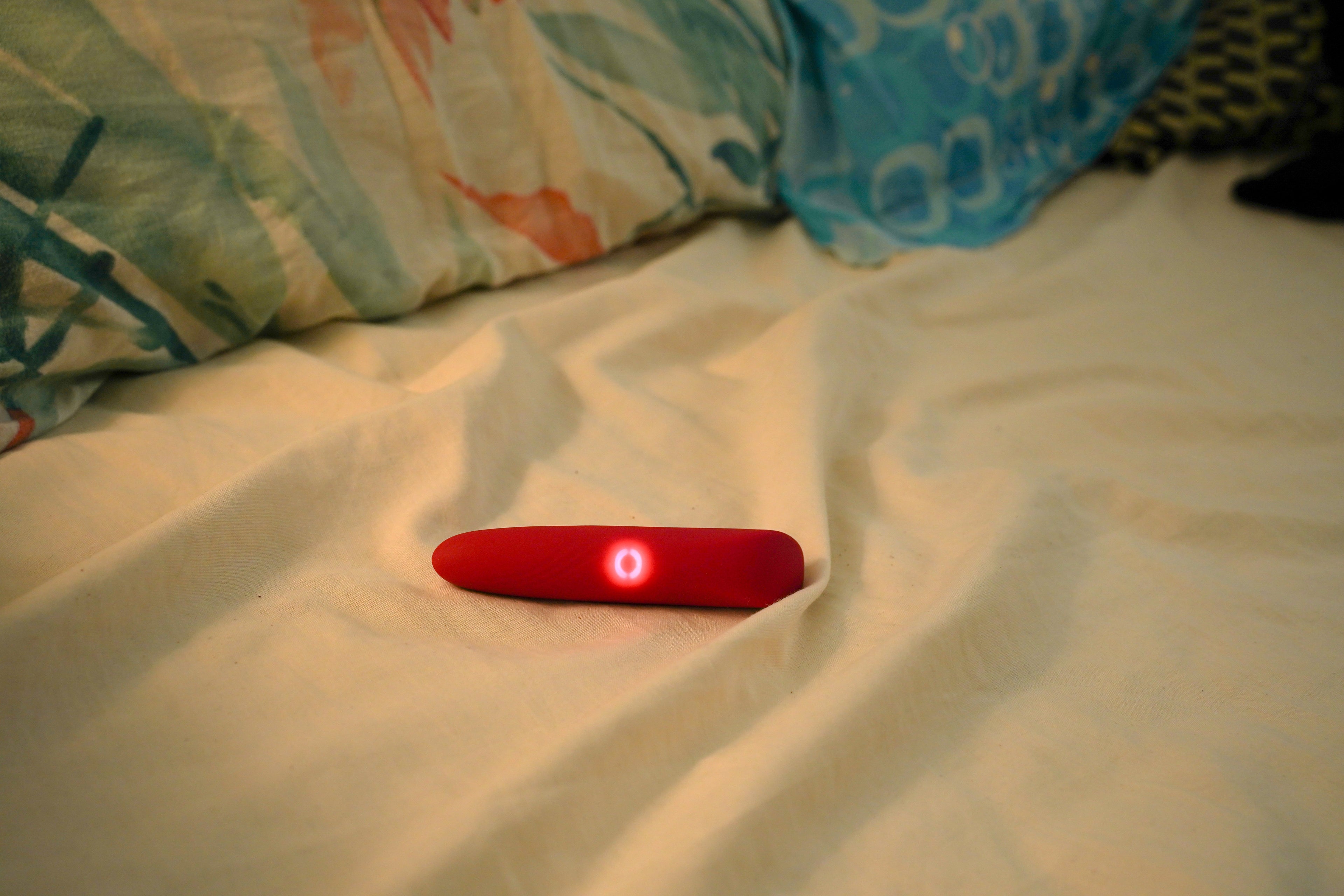 Red light-emitting wellness massager device on a bed with pillows in the background