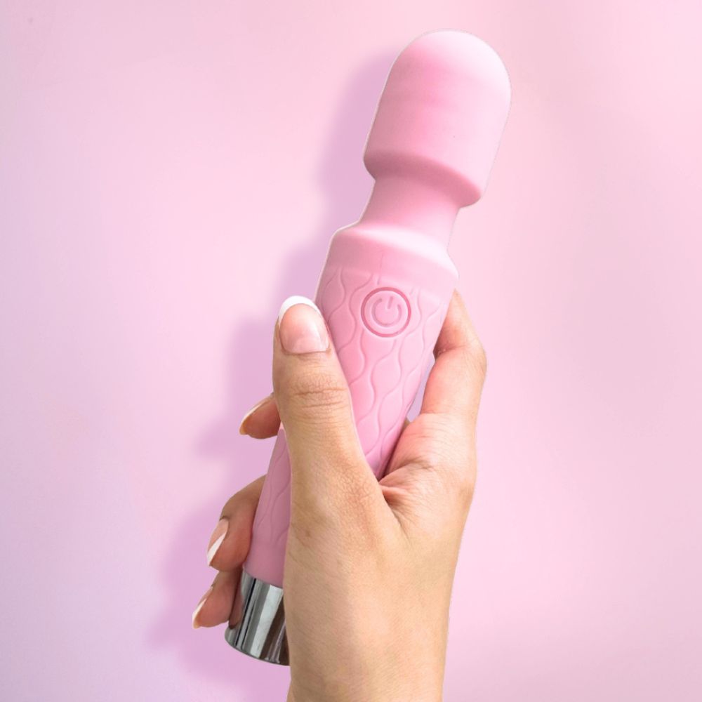 Pink handheld massager held by a hand against a pink background, smooth finish, premium look