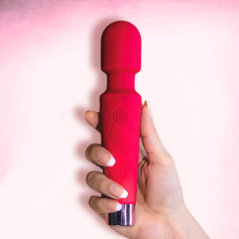 Red handheld massaging device held in a hand against a pink background