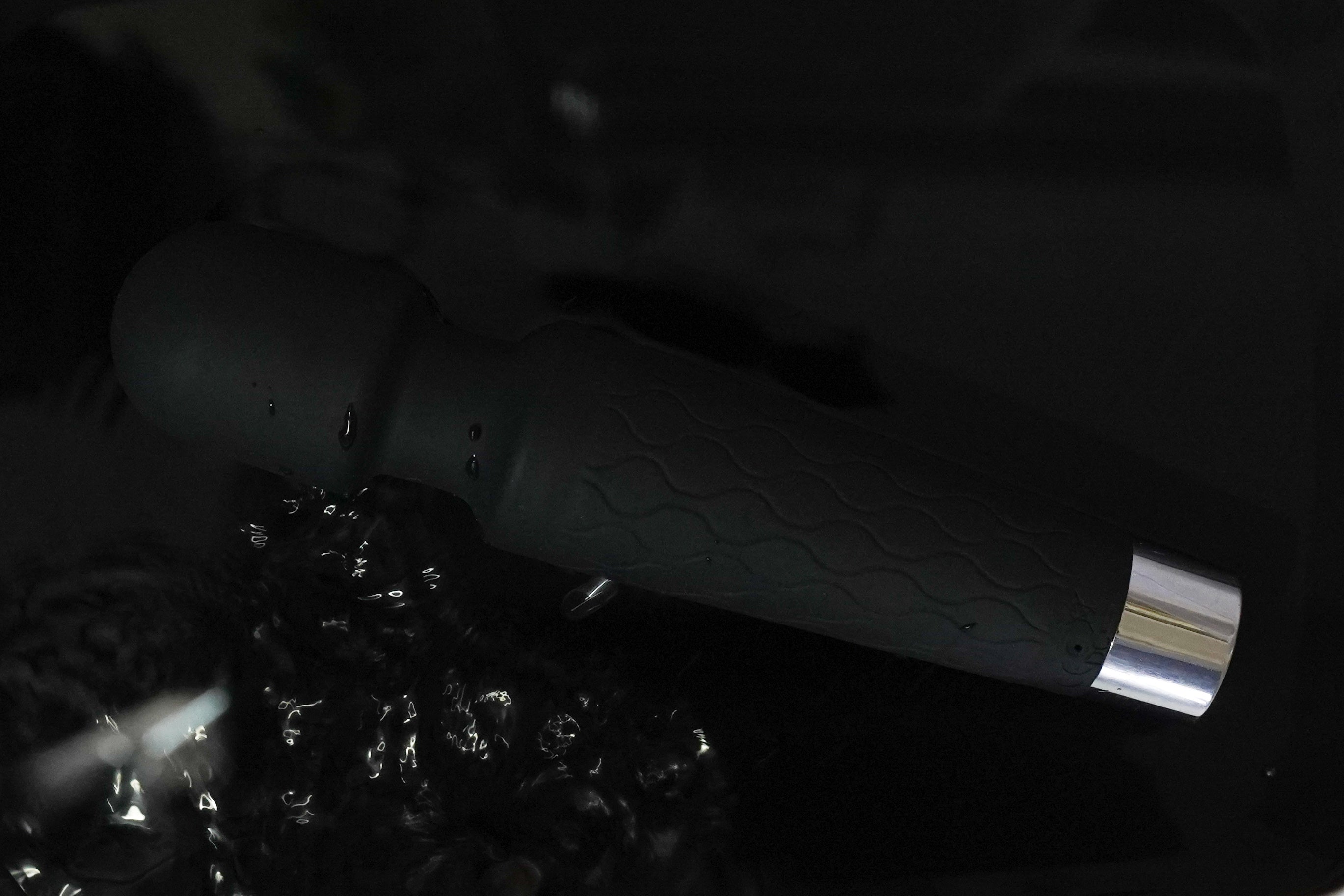 Close-up of a smooth personal handheld massager with water droplets on a dark and watery background